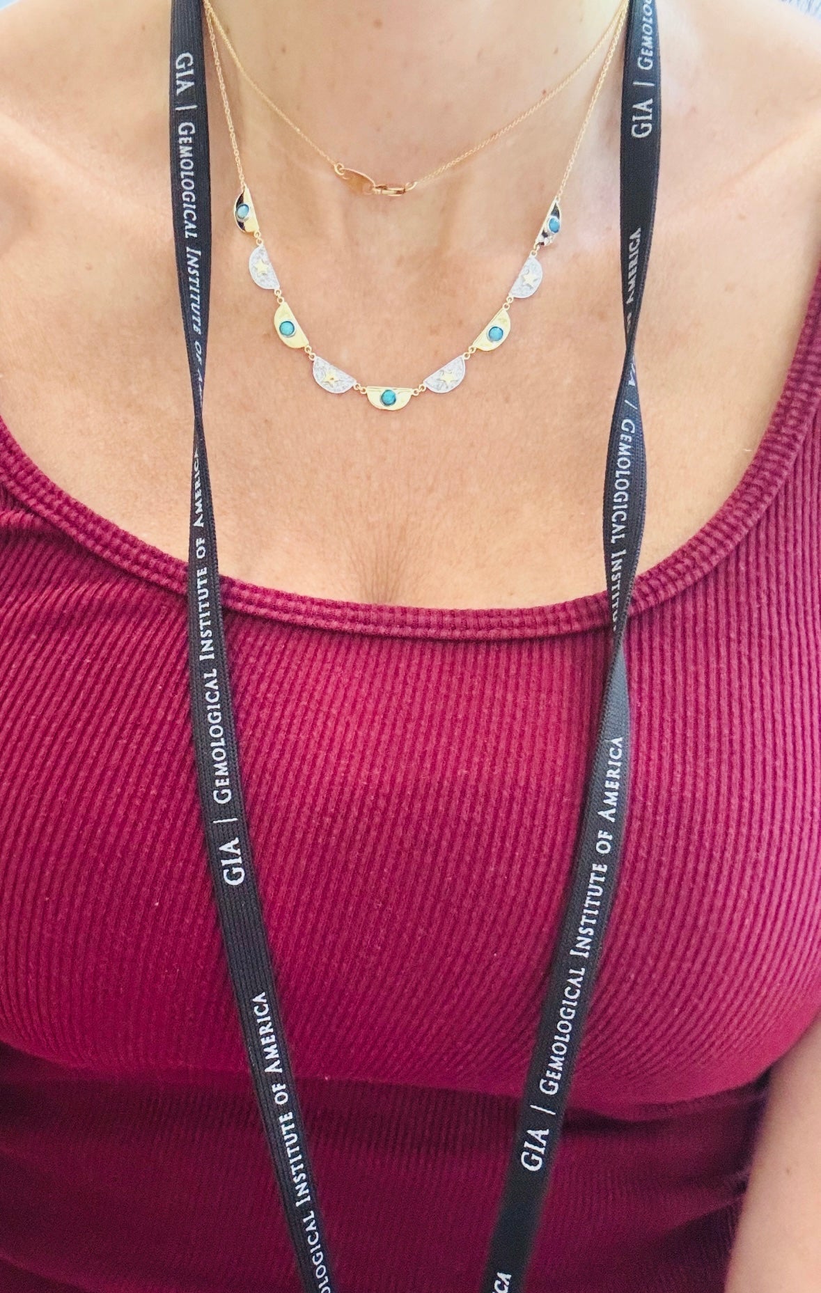 Woman wearing a scalloped gold necklace and a GIA badge.