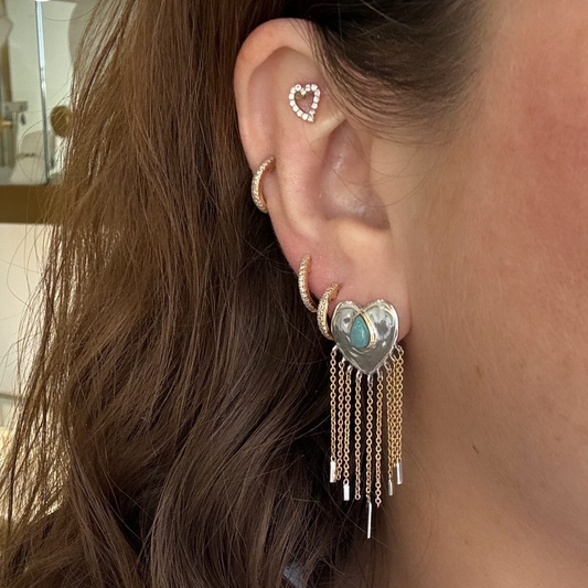 Close-up of an ear wearing a heart-shaped earring with tassels.